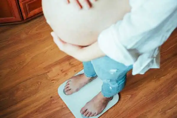Image of woman weighing herself and experiencing weight gain through pregnancy Clydebank